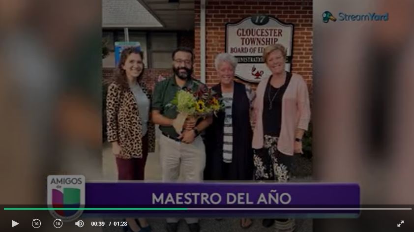 screenshot of video: Angel Santiago, standing in between three women, holding a bouquet of flowers in front of the Gloucester Township Board of Education building.